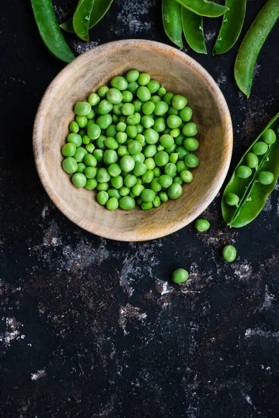 黒荒地に生の緑のエンドウ豆の木製のボウルとポッド — ストック写真