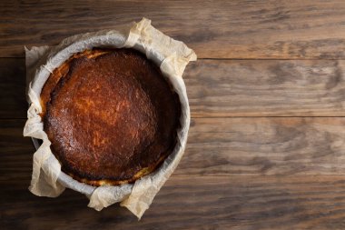 Geleneksel Bask peynirli keki pişirme kalıbında kırsal ahşap bir masa üzerinde pişirme kağıdıyla yaktı.