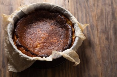 Geleneksel Bask peynirli keki pişirme kalıbında kırsal ahşap bir masa üzerinde pişirme kağıdıyla yaktı.