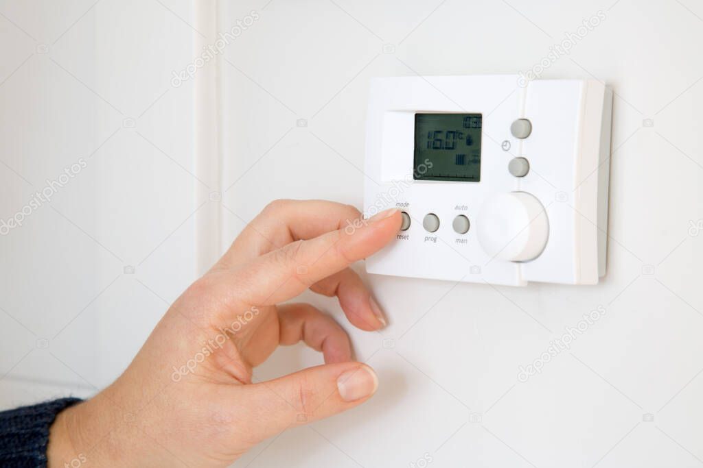 Woman hand adjusting digital central heating thermostat at home