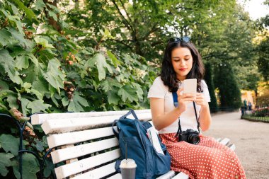 Şehir parkında oturan akıllı telefonunu kullanan güzel bir turist kadın.