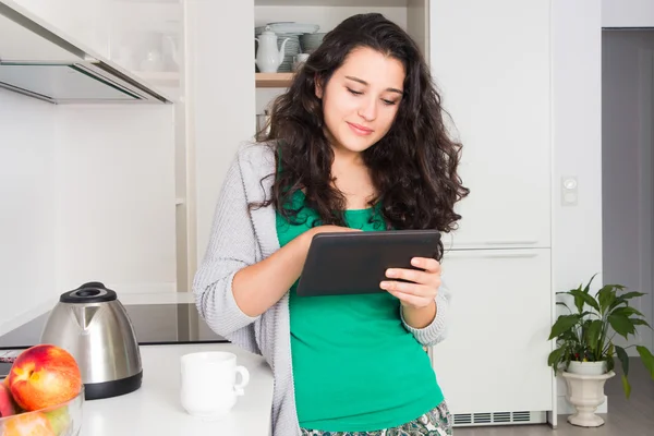 Jovem mulher usando um tablet em sua cozinha — Fotografia de Stock