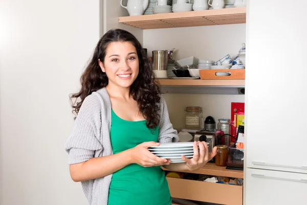 Молодая женщина достает посуду из шкафа, чтобы накрыть на стол — стоковое фото