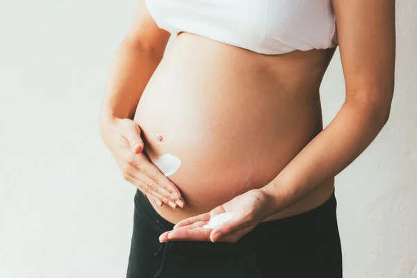 Gravid kvinna tillämpa fuktighetskräm på magen — Stockfoto