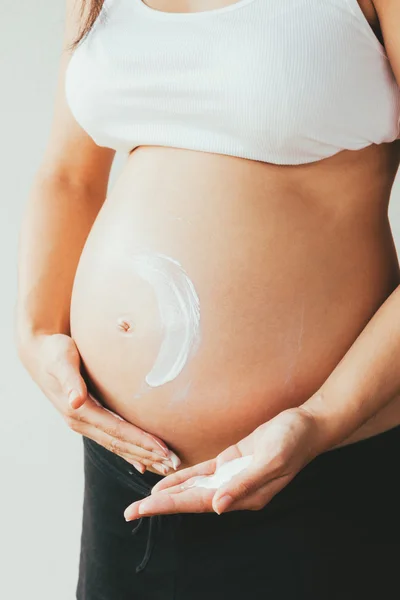 Беременная женщина наносит увлажняющий крем на живот — стоковое фото