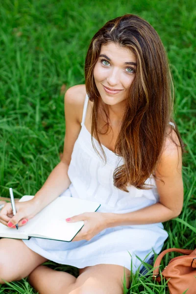 Otların arasında oturan bir defter yazma kız — Stok fotoğraf