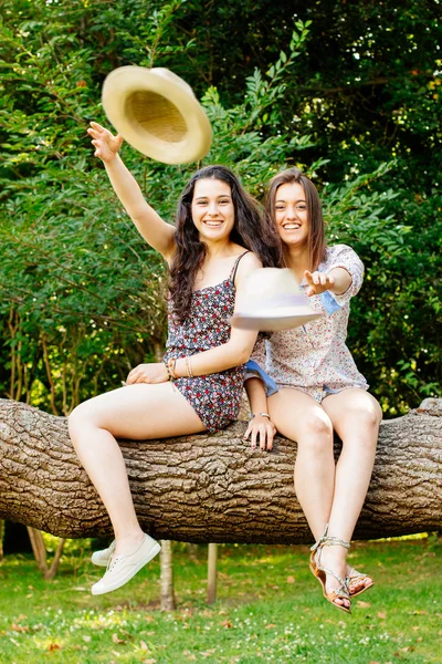 Girl frinds sitting on a trunk throwing hats — Stock Photo, Image