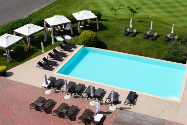 Güneşli bir yaz gününde havuzun mavi suyu, güneş pansiyonları ve şemsiyeleri manzarası.