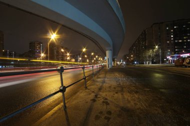 Gece otoyolu üst geçidi, uzun pozlama fotoğrafı, farların sarı çizgileri.