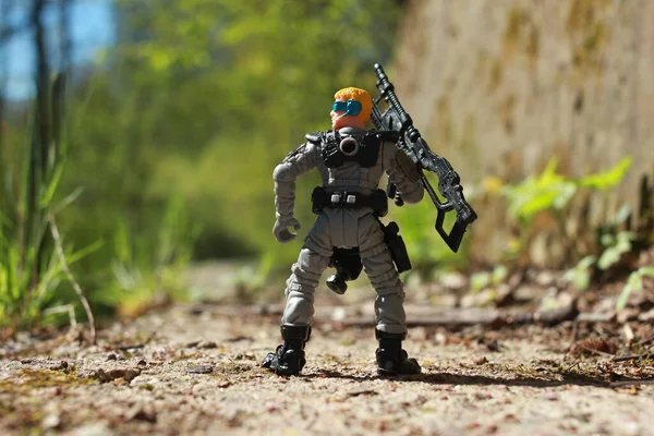 A toy figure of a military soldier with a machine gun in his hands with his back in the green strip of the tropics