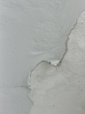 Açık gri bir boyanın yakın çekimi eski bir duvarı soyuyor ve pul pul döküyor. Altındaki pürüzlü, dokulu bir yüzeyi ortaya çıkarıyor. Bu yıpranmış detay aşınmayı, hasarı ve soyut kalıpları gösteriyor, arka plan kullanımı için mükemmel..