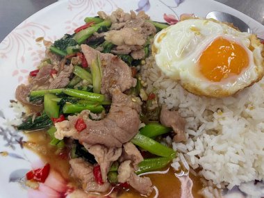 Kızarmış domuz eti, çıtır Çin brokolisi, kırmızı biber ve üzerine beyaz pirinç serpiştirilmiş mükemmel bir kızarmış yumurta içeren popüler bir Tayland yemeğinin yakın çekimi..