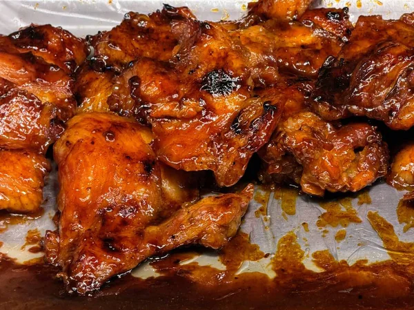 Yumuşak, sulu ızgara tavuk butları. Parlak, tatlı ve lezzetli bir sosla güzelce yağlanmış. Metal bir tepside sunuluyor..