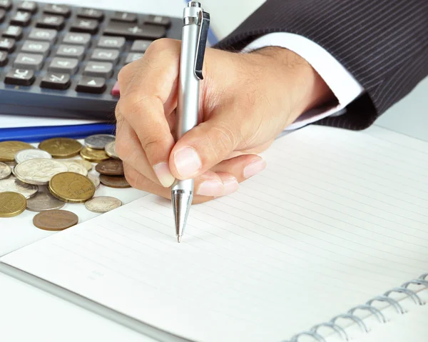 Businessman hand holding a pen writing on empty paper with coins — Stock Photo, Image