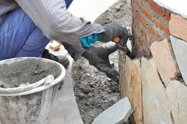 Рабочий каменщик устанавливает надгробия на кирпичной стене — стоковое фото