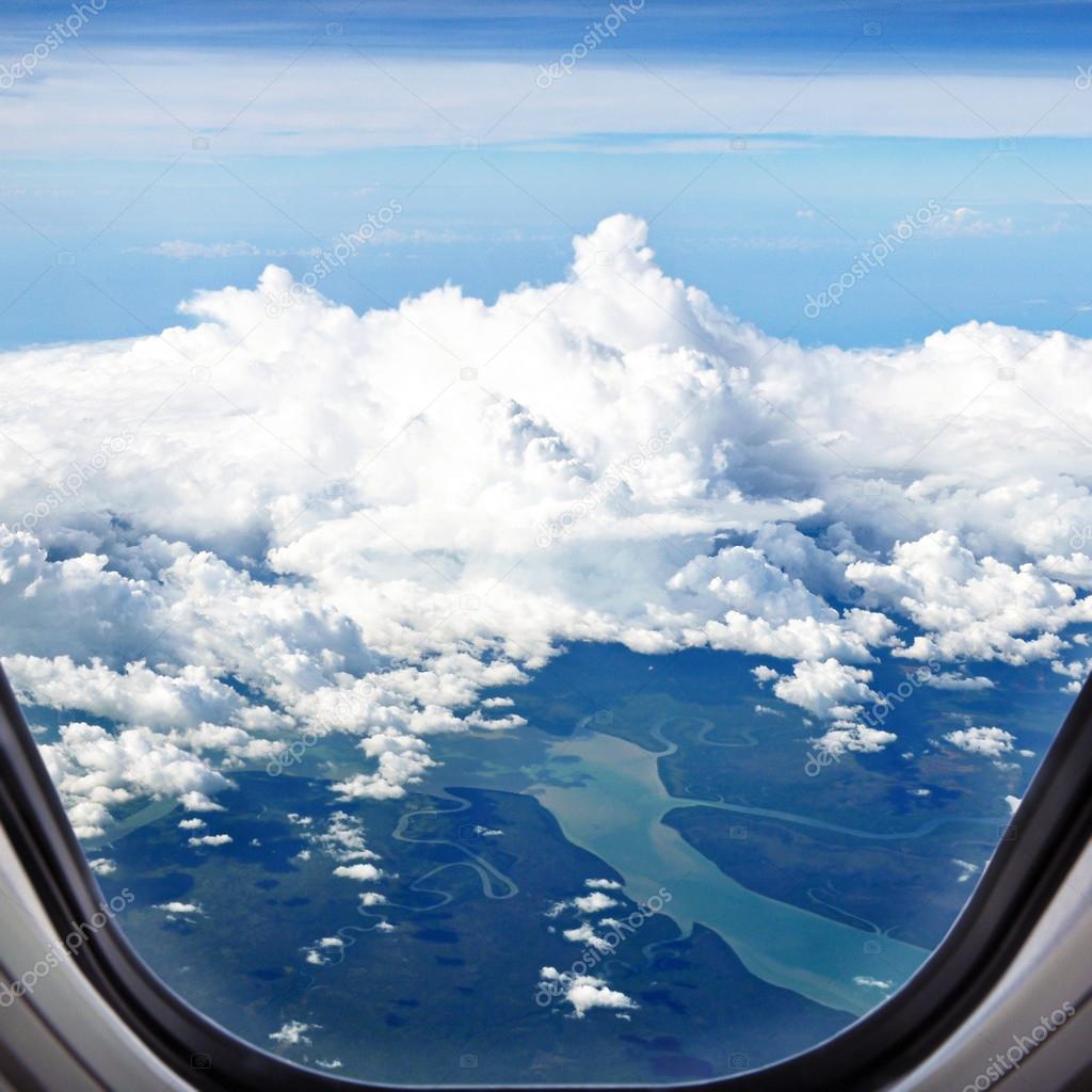 Aerial view of land and rivers covered with clouds - from window of the airplane