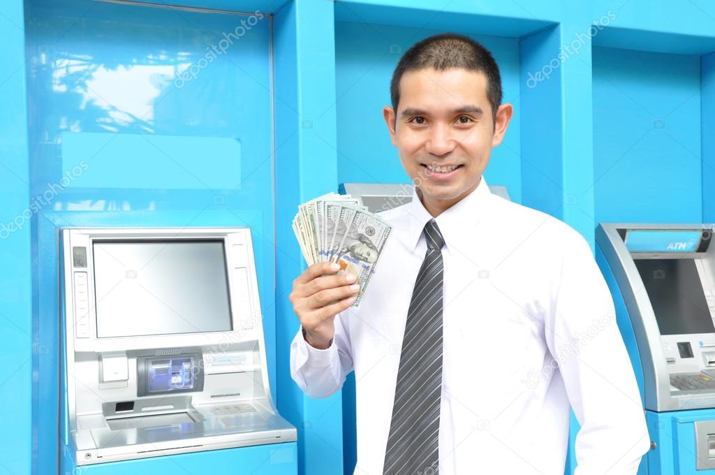 Businessman holding money near ATM