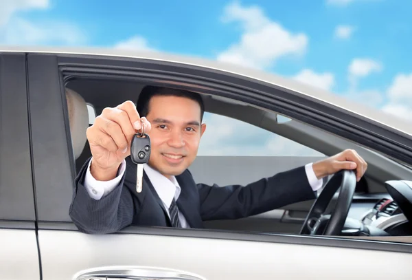 Asiatische Geschäftsmann als Fahrer zeigt einen Autoschlüssel auf blauem Himmel Hintergrund — Stockfoto