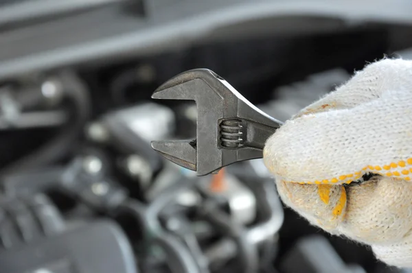 Hand wearing glove holding wrench in front of car engine — Stock Photo, Image