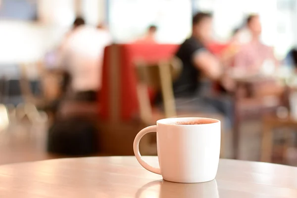 Xícara de café na mesa com pessoas na cafeteria como fundo borrão — Fotografia de Stock