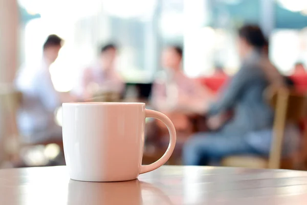 Coffee cup on the table with people in coffee shop as blur background