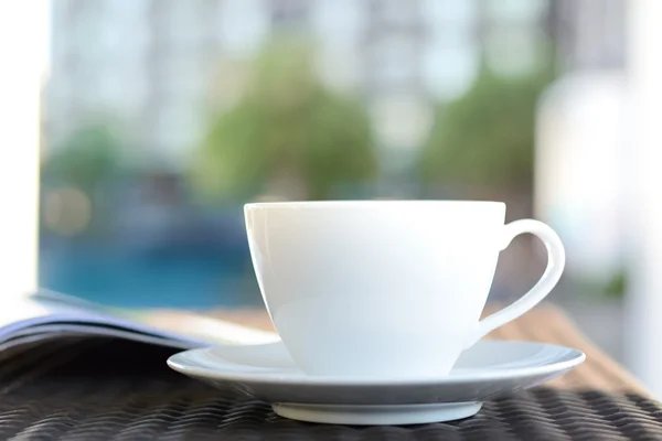 Tasse à café avec livre sur la table dans un bâtiment flou & fond de plante verte — Photo