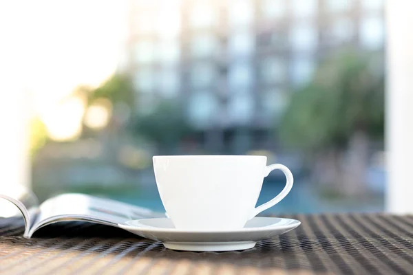 Tasse à café avec livre sur la table dans un bâtiment flou & fond de plante verte — Photo