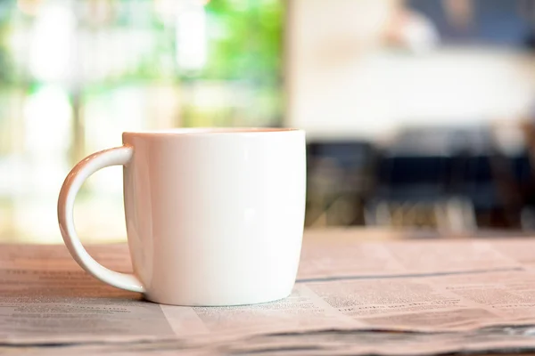 Taza de café sobre el periódico en la mesa en el fondo borroso de la cafetería —  Fotos de Stock