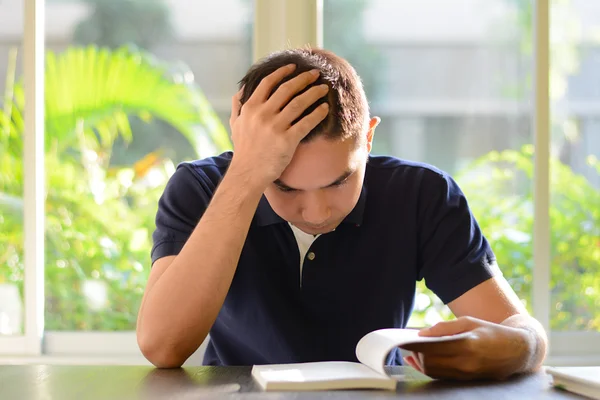 Young man reading book with hand on his head — Stock Photo, Image