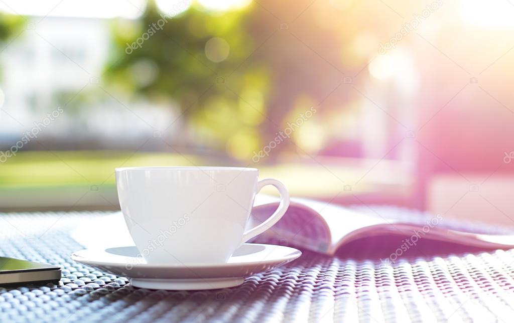 Coffee cup with book on blurred green nature background