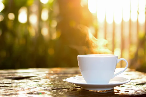 Hett kaffe i koppen på gamla bord av trä med solljus & oskärpa gre — Stockfoto