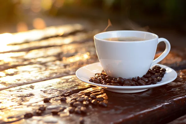 Café chaud dans la tasse sur une vieille table en bois avec des grains de café — Photo