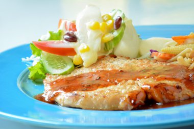 Pan kızarmış domuz biftek renkli mavi plaka üzerinde karışımı sebze salatası ile