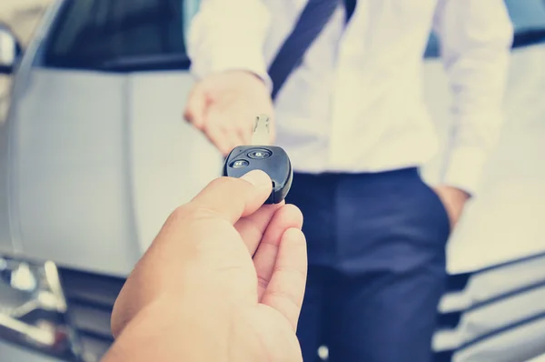 Hand giving car key to a man with car background - vintage tone — Stock Photo, Image