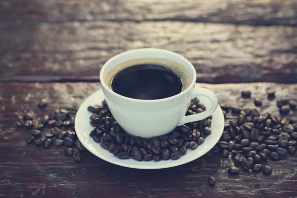 Café preto na xícara na mesa de madeira velha com grãos de café — Fotografia de Stock