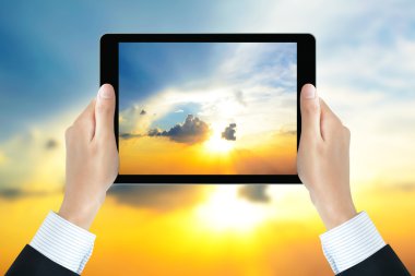 Businessman hands holding tablet pc, taking picture of the sun shining in the sky