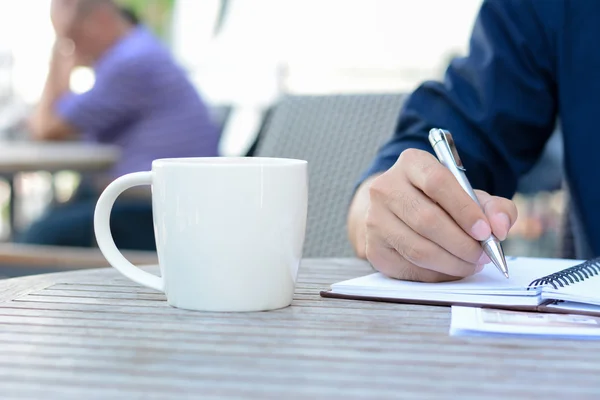 Ręką człowieka pisania na notebooka z filiżanki kawy obok — Zdjęcie stockowe