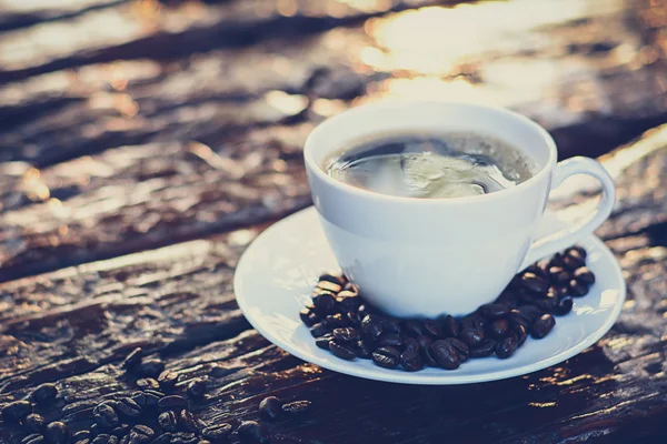 Café negro en la taza en la mesa de madera vieja con granos de café — Foto de Stock