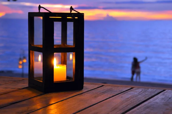 Linterna de vela con pareja en la playa como fondo —  Fotos de Stock