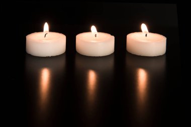 Siyah arka plandaki yansımalarıyla aynı hizada üç beyaz yanan çay lambası.