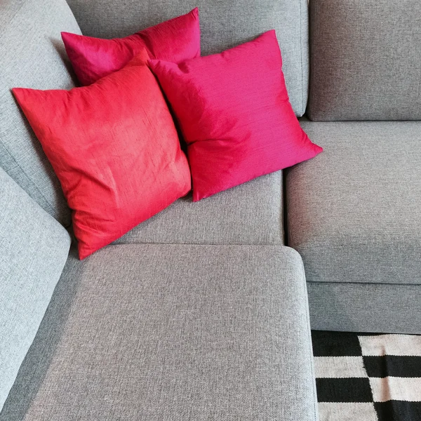 Серый угловой диван с шелковистыми красными подушками — стоковое фото