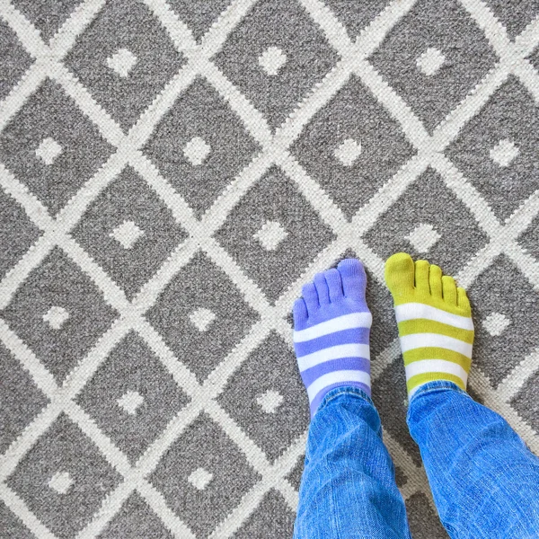 Nogi w niedopasowanych skarpetki na szary dywan — Zdjęcie stockowe