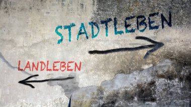 Almanca 'nın iki farklı yönünü gösteren işaret direği olan bir resim. Bir yön şehir yaşamını gösteriyor, diğeri de kırsal yaşamı..