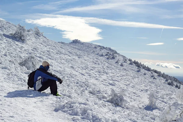 冬の晴れた日に雪景色のパノラマビューを検討雪の山の中に座っているハイキングバックパックを持つ男 彼はマスクをしている スポーツとアクティブな自然生活の概念 — ストック写真