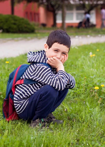 School kind gehurkt op gazon als front van school — Stockfoto