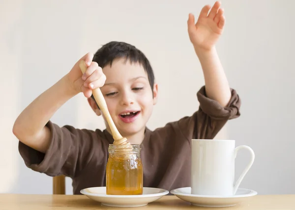 Child adding honey in cup of tea — Stock Photo, Image