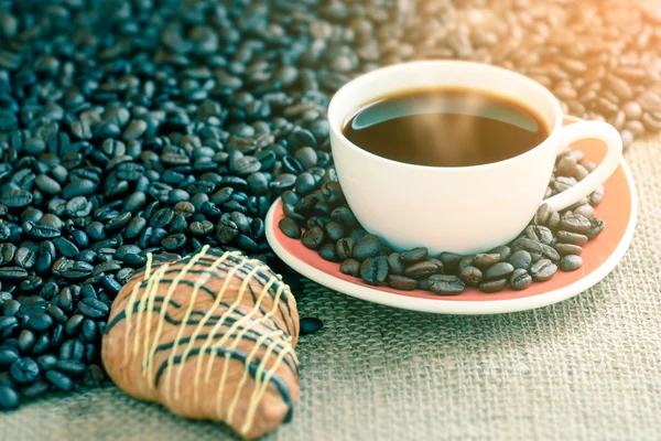 Coffee cup and bread on sack with coffee bean, focused on a cup. — Stock Photo, Image