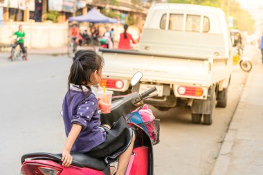Lovely girl drinking a juice while waiting her mother on motorcy