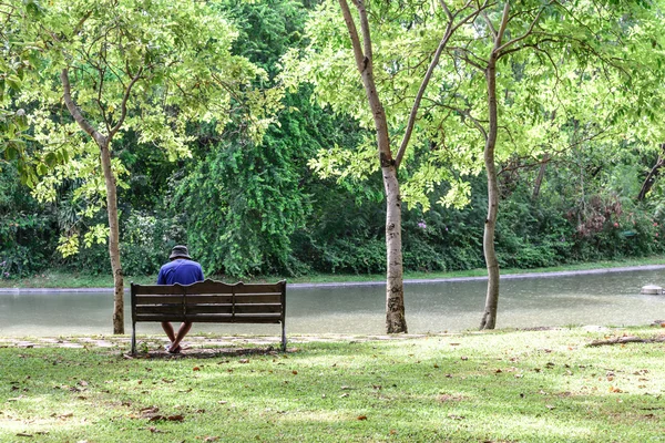 Alleen man in blauw shirt met hoed zittend op houten bankje in het park — Stockfoto