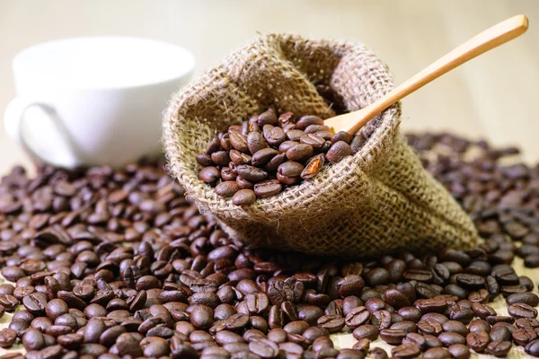 Coffee beans in bag with wooden spoon and cup background. — Stock Photo, Image